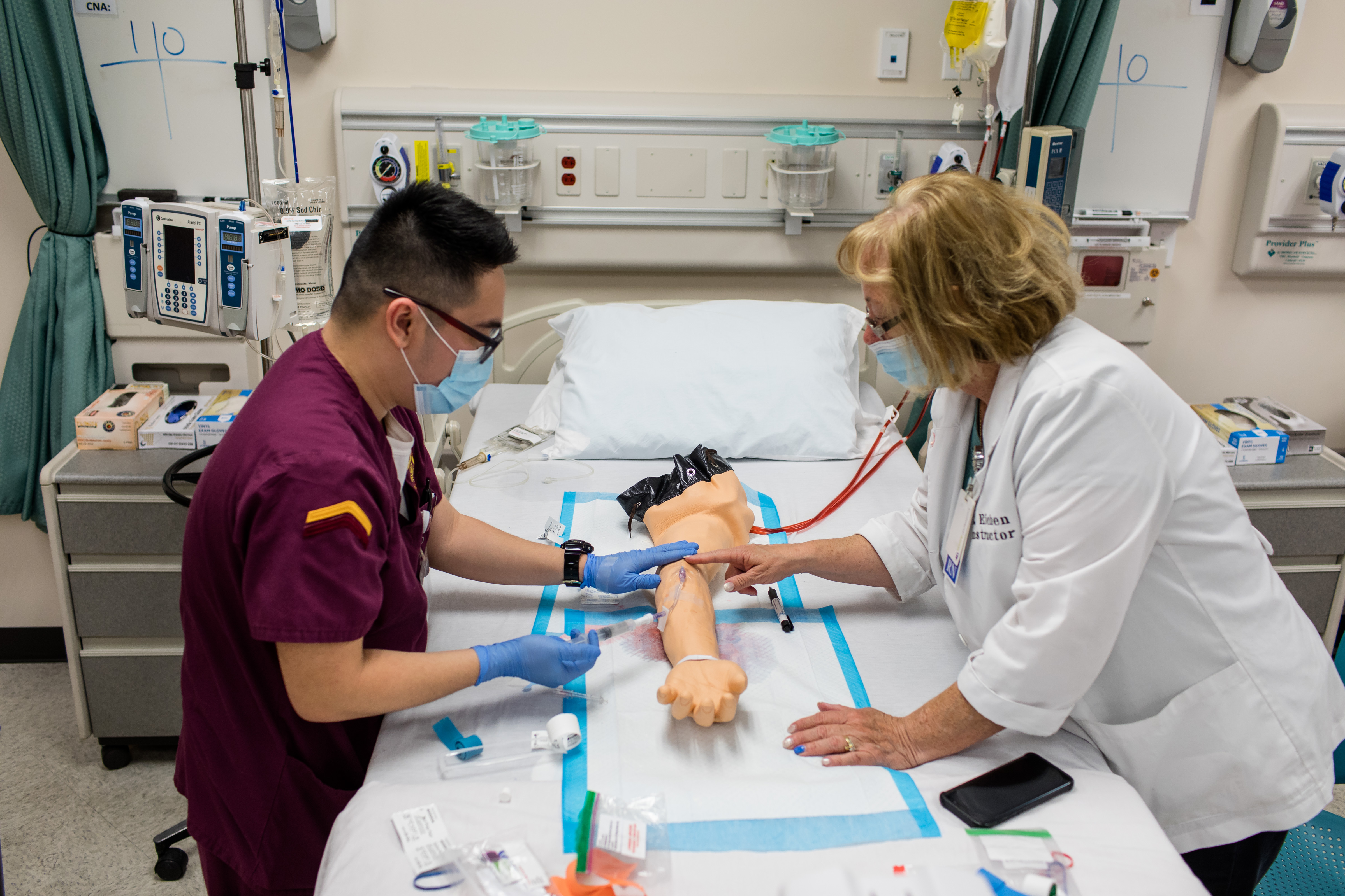 Student and professor working on a dummy arm in lab class.